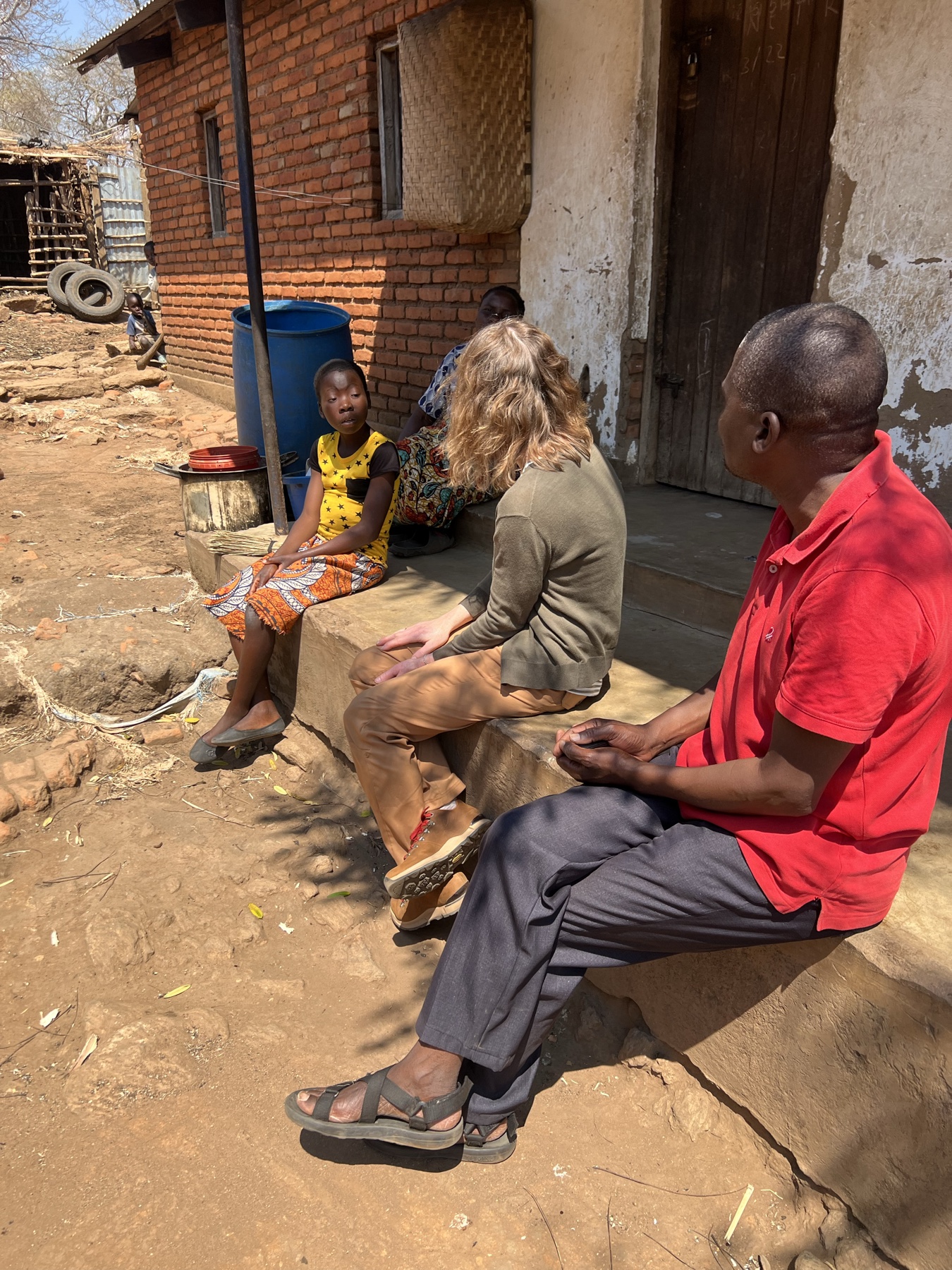 A home visit: ECS sitting with a family outside their home in Malawi