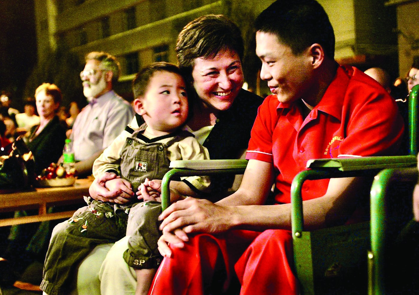 Janice Neilson smiling, with a young boy on her lap and a young man in a red shirt beside her