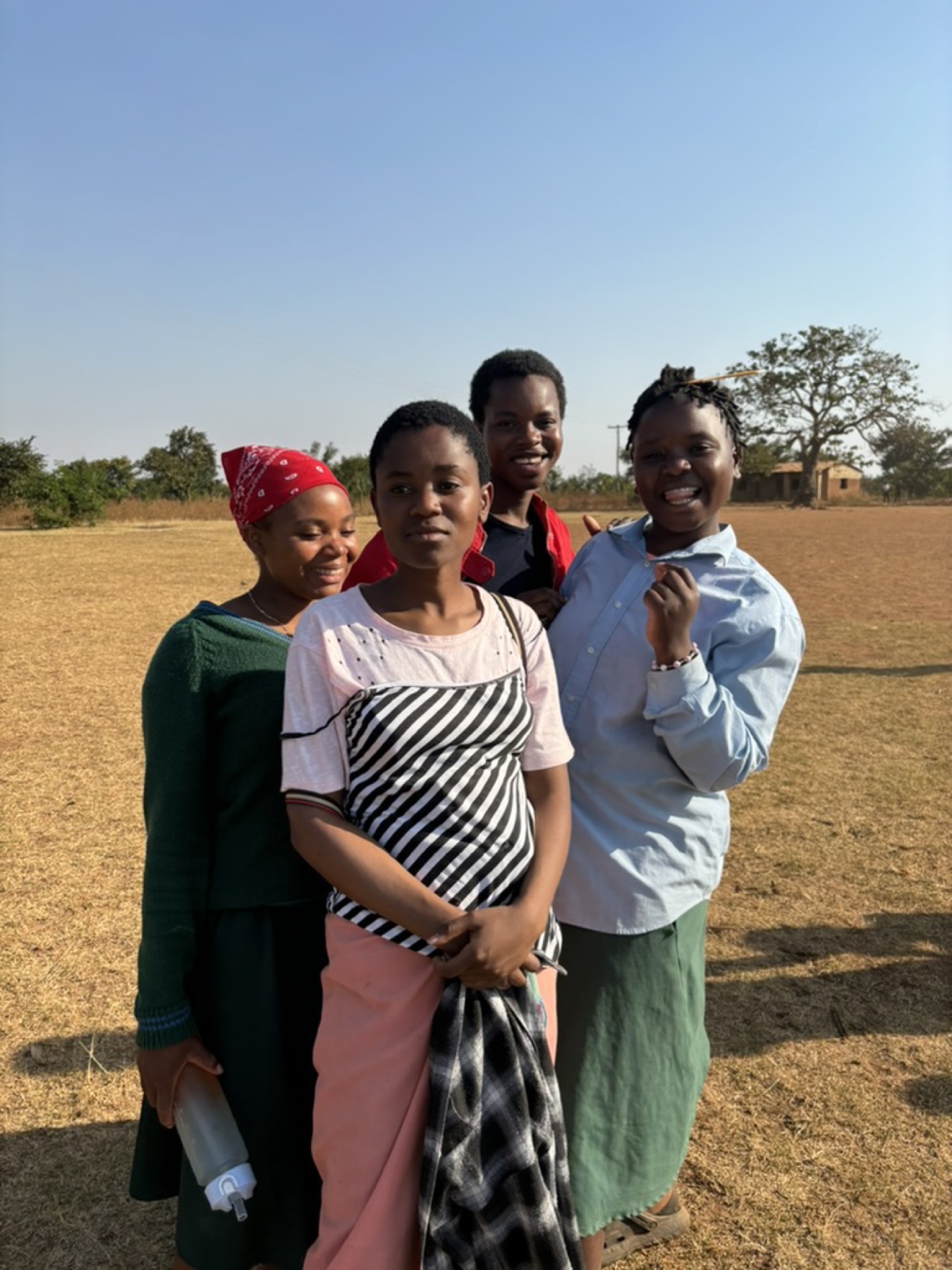 Four young people standing together outside a partner school in Malawi